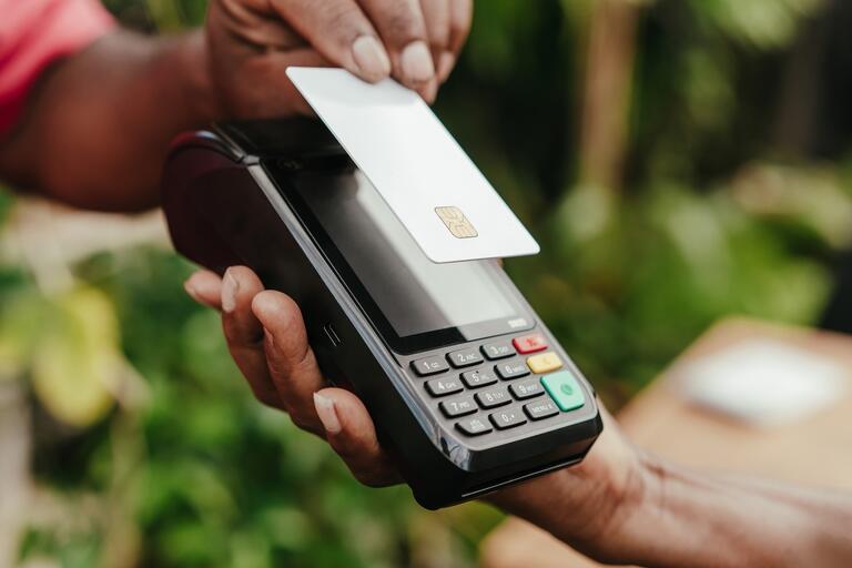 photo of someone holding a pos system and another person paying with a debt/credit card using tap to pay