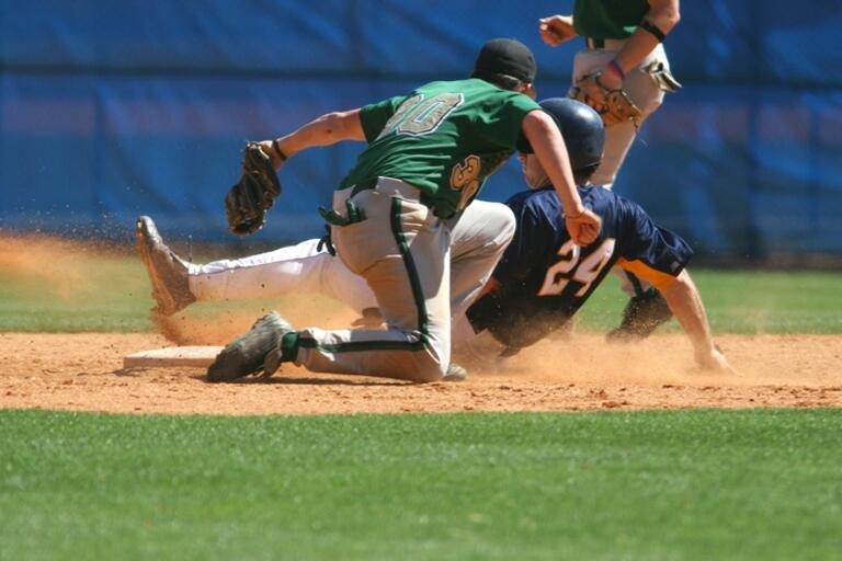 baseball player sliding into base, while baseman tries to tag him out 