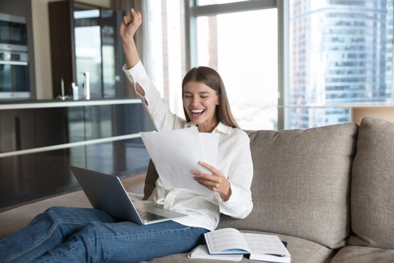 woman excited while looking at a paper and has a laptop open on her lap.