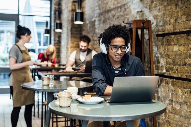 young man at cafe with headphones and laptop open.